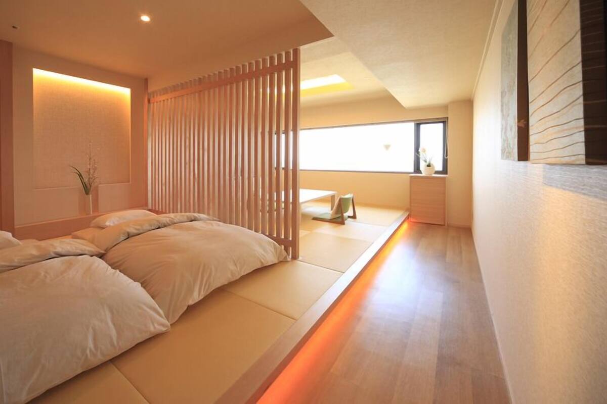 A minimalist room with a low bed, a sliding partition, and a view of the sky.
