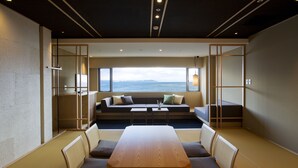Ein modernes Interieur mit einem großen Holztisch und Stühlen, einer Couch mit Kissen und Meerblick durch große Fenster.