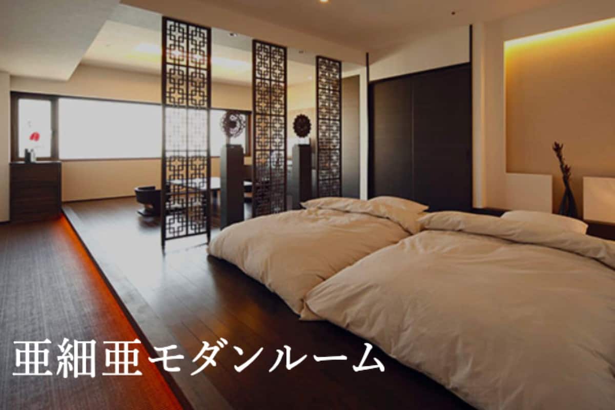 Ein modernes Schlafzimmer mit einem großen Bett, Holzboden und einem dekorativen Raumteiler.