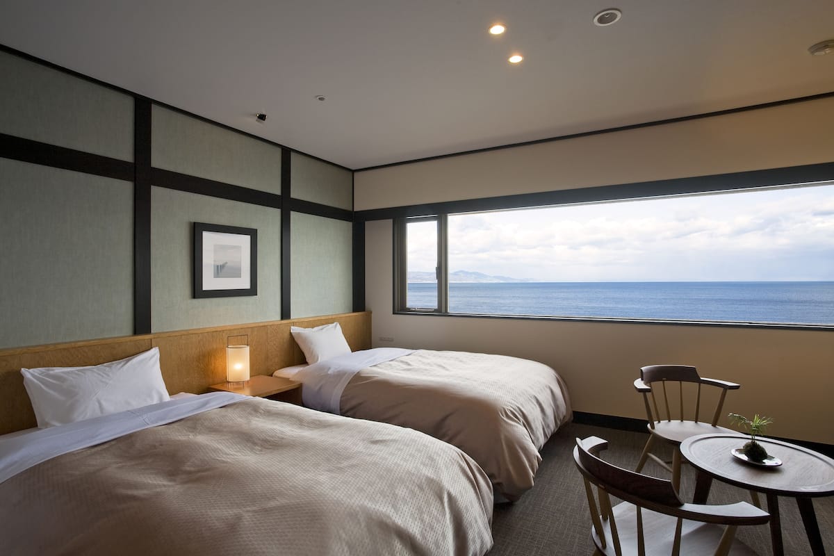 Ein Hotelzimmer mit zwei Betten, einem kleinen Tisch und Blick auf das Meer.