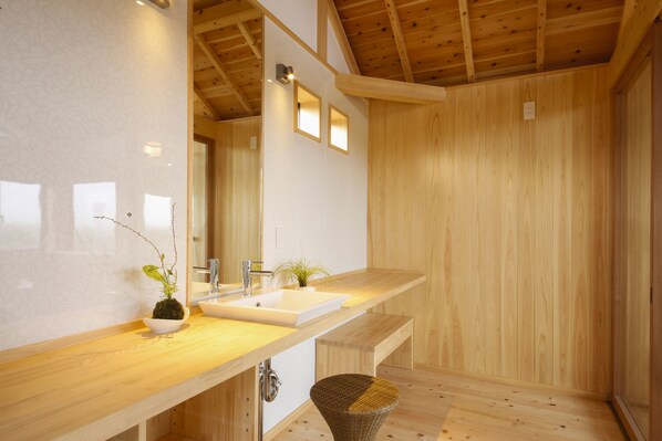 A modern bathroom with wooden walls and a wooden ceiling. It includes a sink, a mirror, and a small plant.