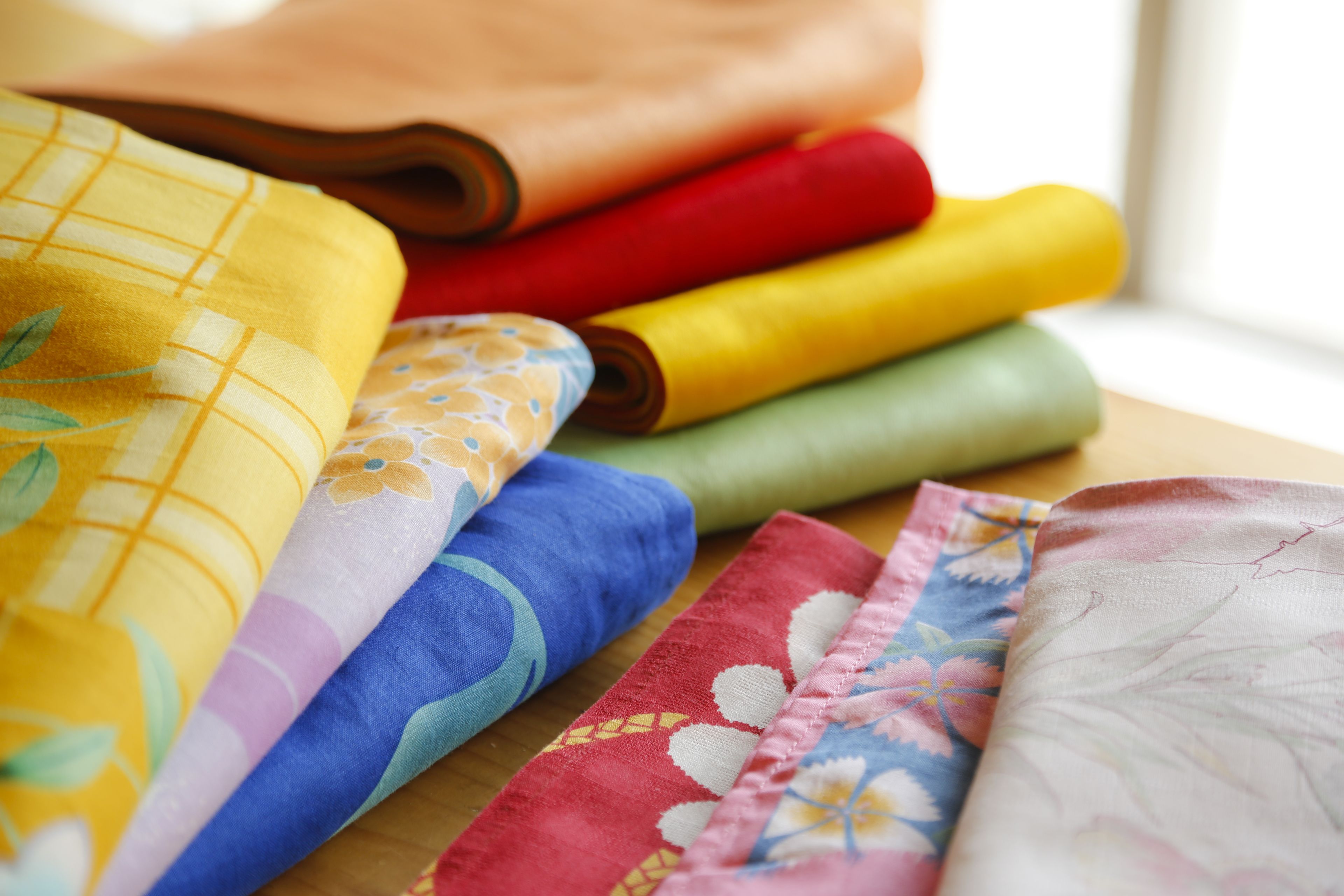 A variety of colorful fabrics laid out on a wooden surface.