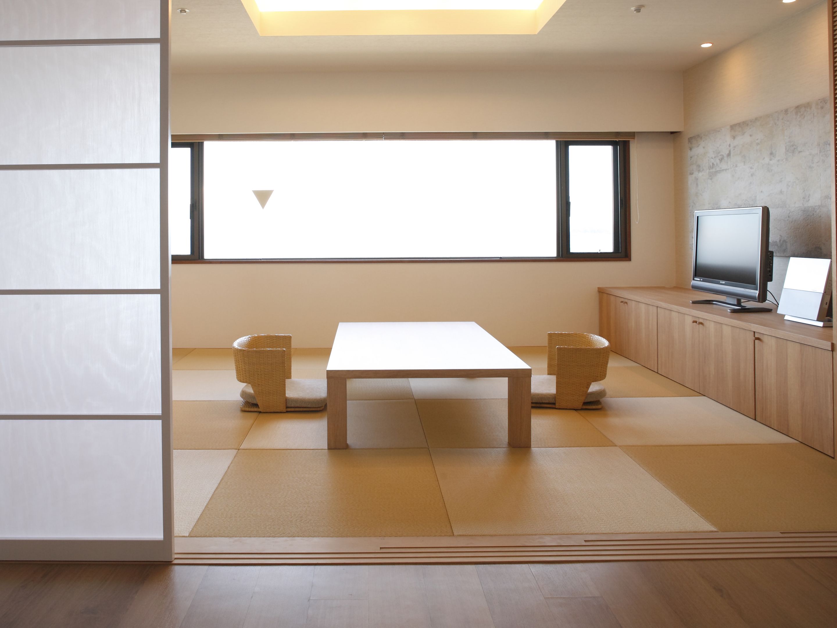 A modern room with a large window, a wooden table, two chairs, a television, and a cabinet.