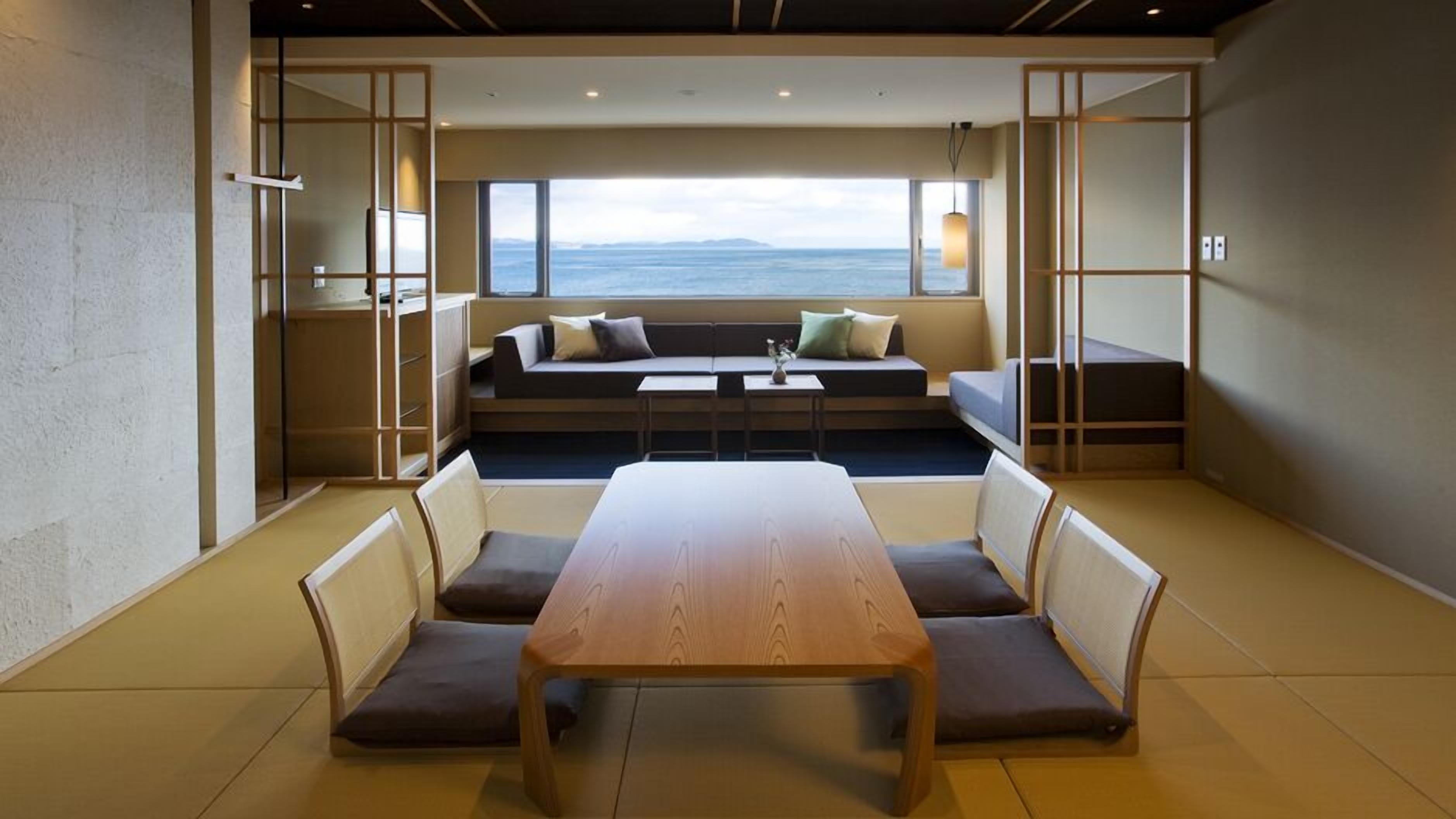 Un intérieur moderne avec une table et des chaises en bois, un canapé avec des coussins et une vue sur la mer grâce à de grandes fenêtres.