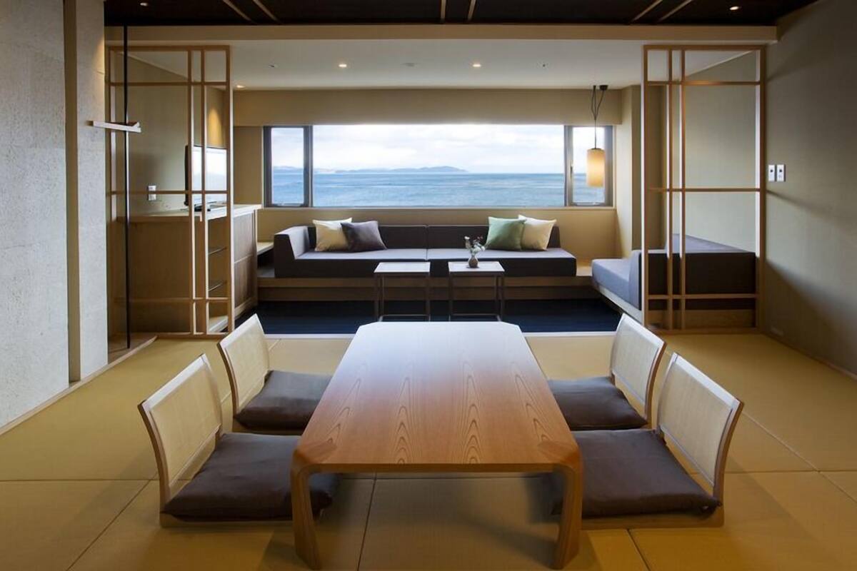 A modern interior with a wooden table and chairs, a sofa with cushions, and a view of the sea through large windows.