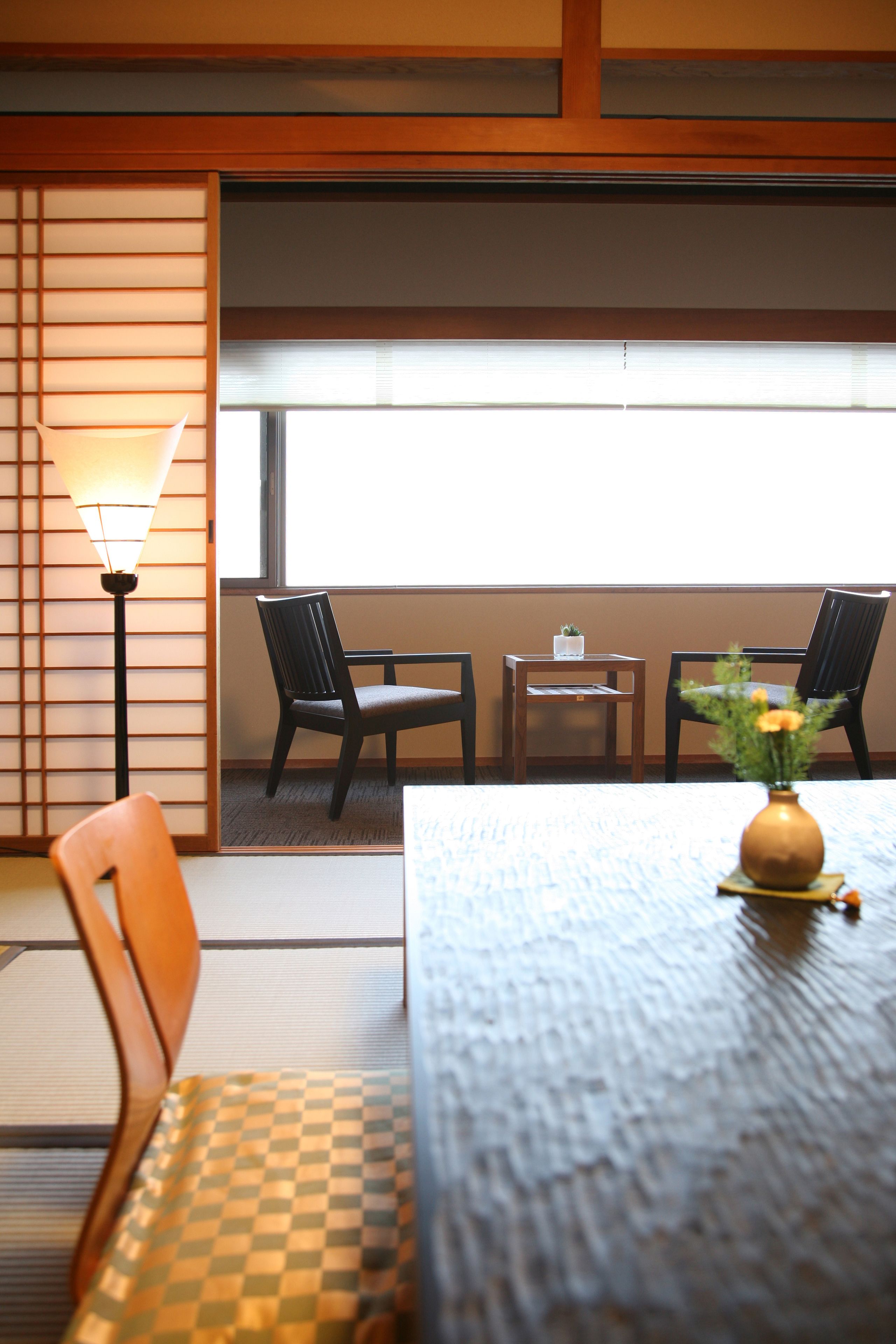 Een traditionele Japanse kamer met tatami vloerbedekking, een lage tafel met een vaas, en twee stoelen.