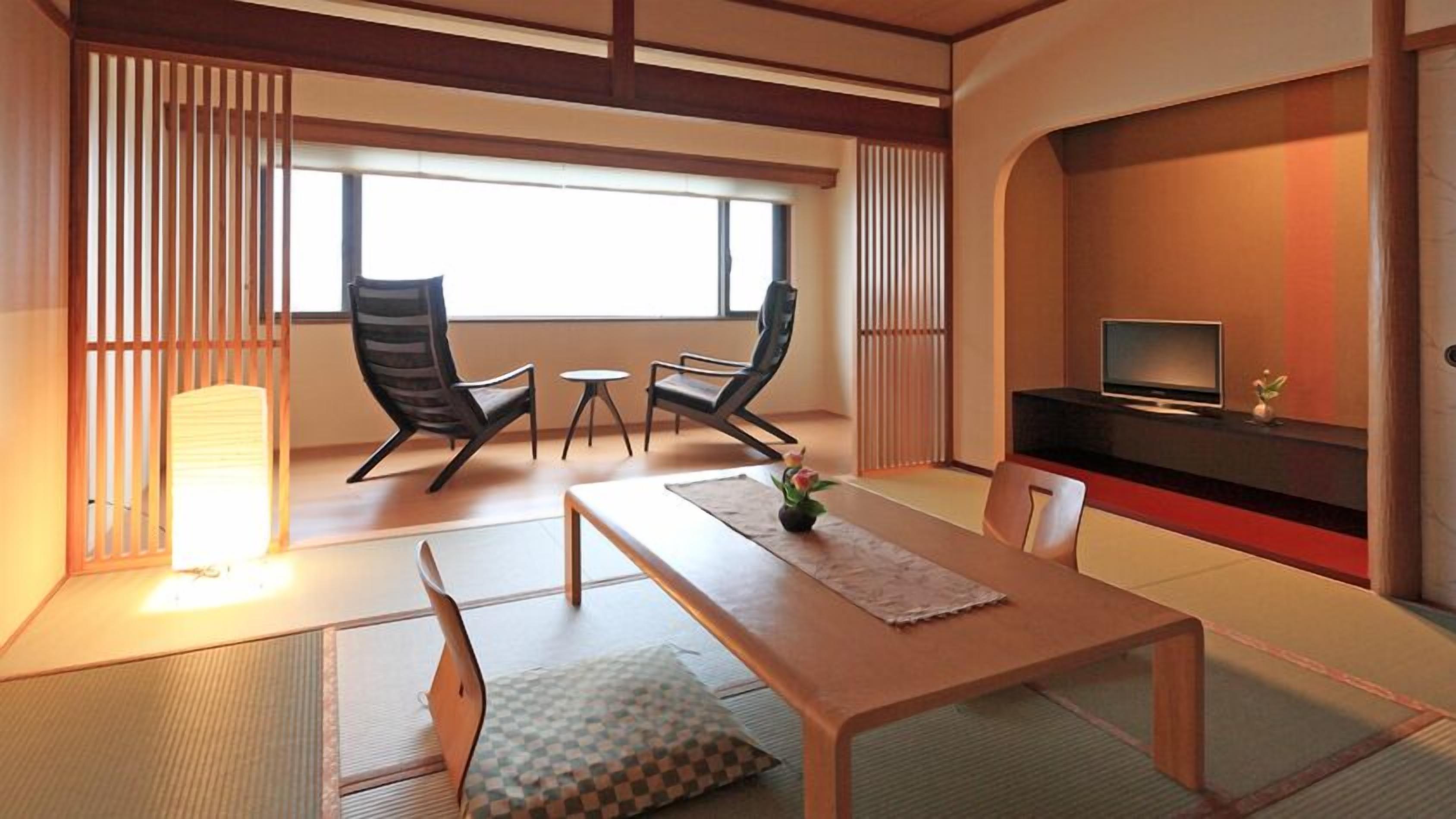 Une pièce de style japonais traditionnel, avec un sol recouvert de tatamis, une table basse, deux chaises, un téléviseur et une porte coulissante.