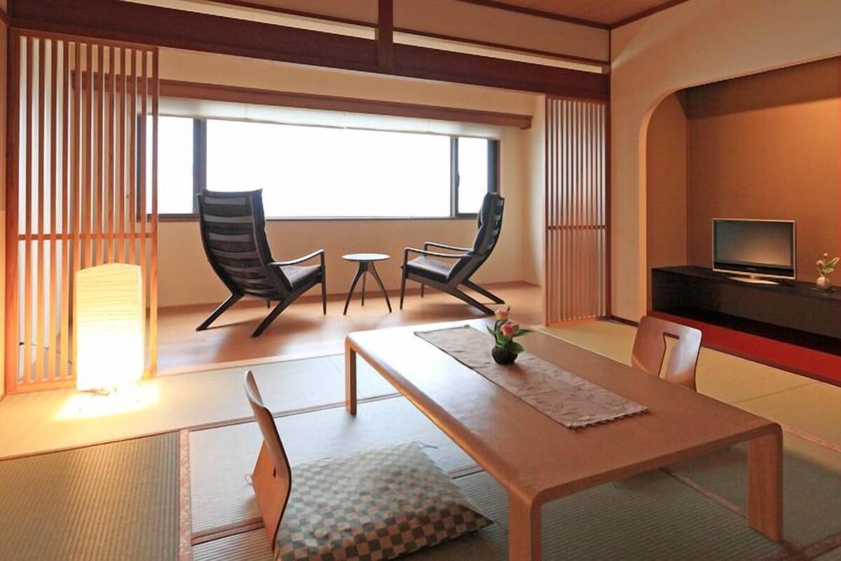 A traditional Japanese-style room with tatami flooring, a low table, two chairs, a television, and a sliding door.