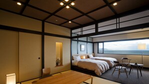 Ein Hotelzimmer mit Tatami-Boden, einem Holztisch, zwei Betten, einem Schreibtisch und Meerblick.