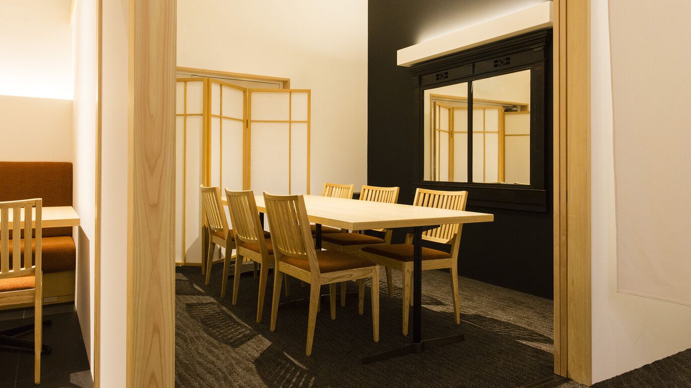 A room with a wooden dining table and chairs, a black-framed window, and a traditional sliding door.