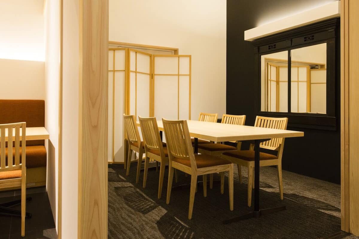 Ein Zimmer mit einem Holzespeisetisch und Stühlen, einem Fenster mit schwarzem Rahmen und einer traditionellen Schiebetür.