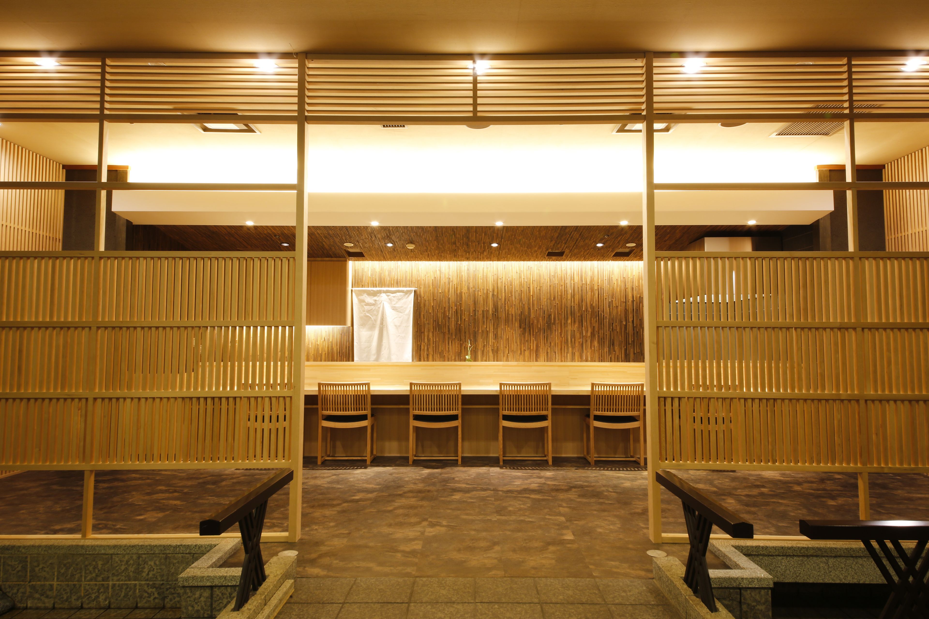 Un interior japonés tradicional con suelo de tatami, separadores de madera y un mostrador de recepción con sillas.