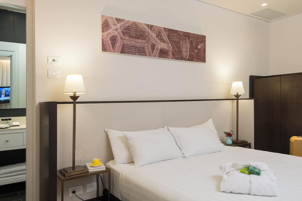A hotel room with a bed, two bedside lamps, a nightstand with a lamp, a television, and a wall-mounted map.