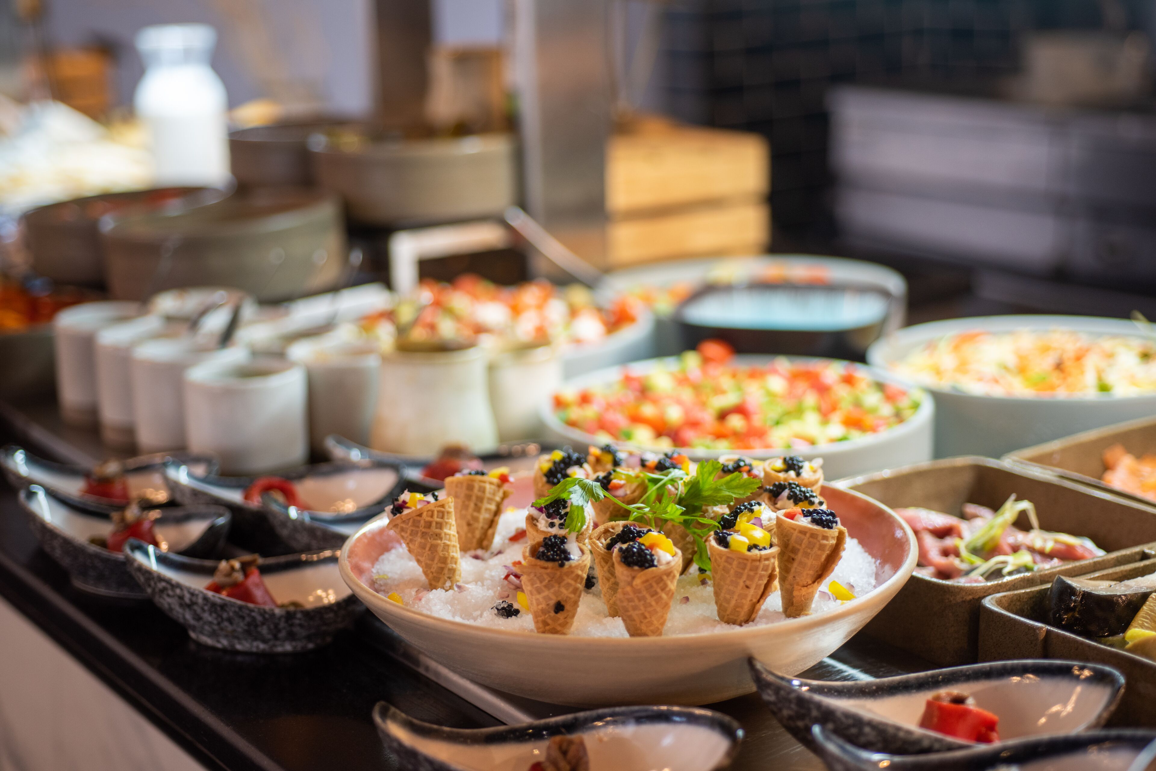 A buffet with various dishes, including waffles topped with berries and cream, and a bowl of salad.