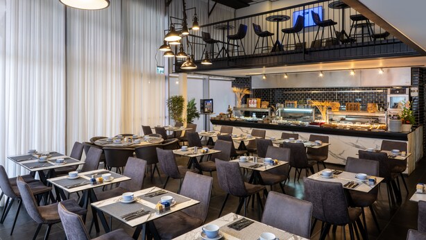 A modern restaurant with multiple dining tables and chairs, a bar area with a counter, and a mezzanine level with seating.