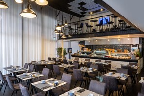 A modern restaurant with multiple dining tables and chairs, a bar area with a counter, and a mezzanine level with seating.