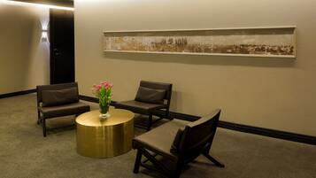 A conference room with a round table, two chairs, a vase with flowers, and a large landscape painting on the wall.