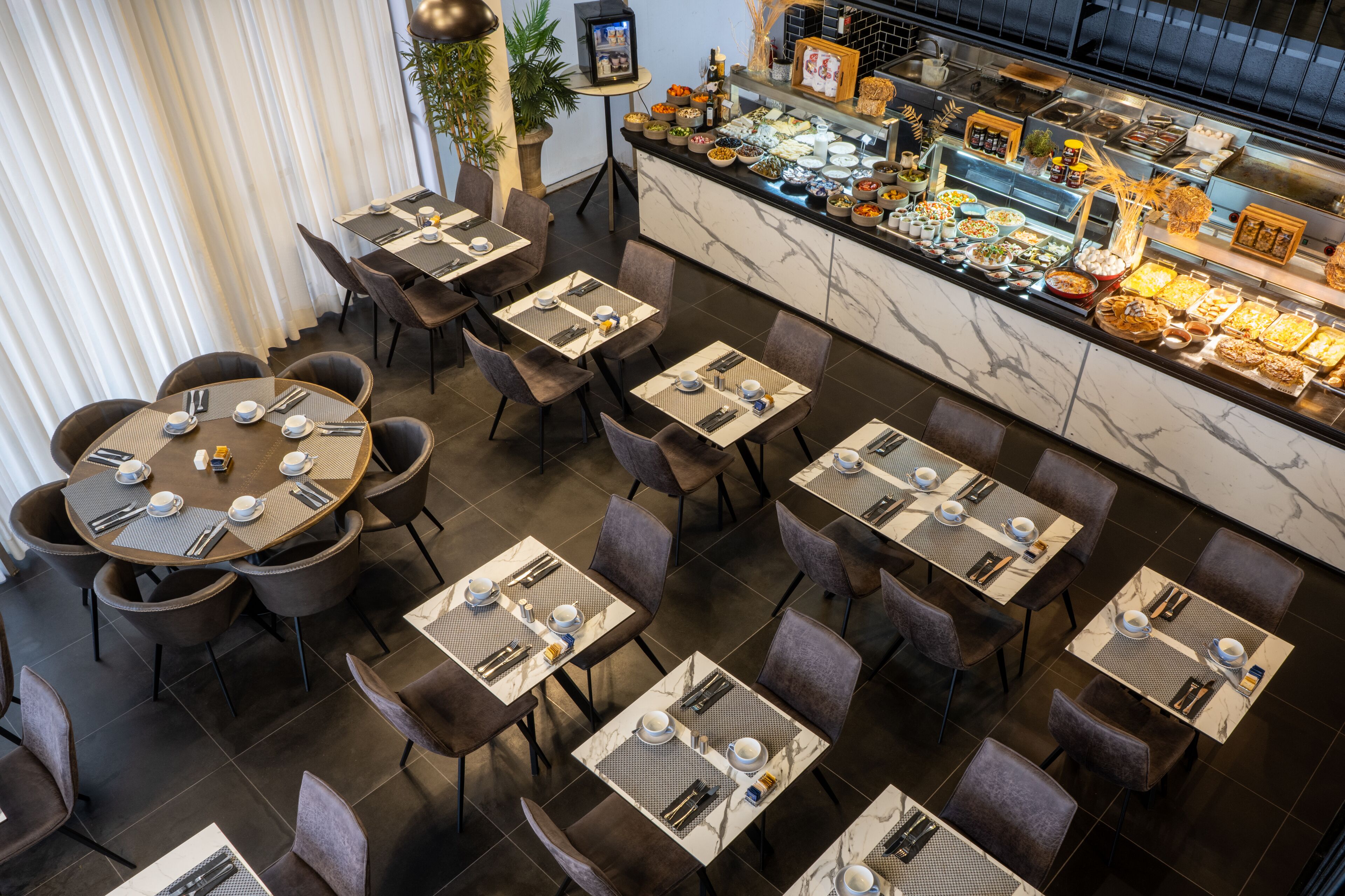 Un restaurant amb diverses taules i caires, un rebost amb diferents plats i una tauletera de marbre.