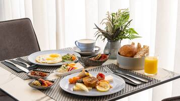 A breakfast table with plates of food, a cup of coffee, a glass of orange juice, and a vase with plants.