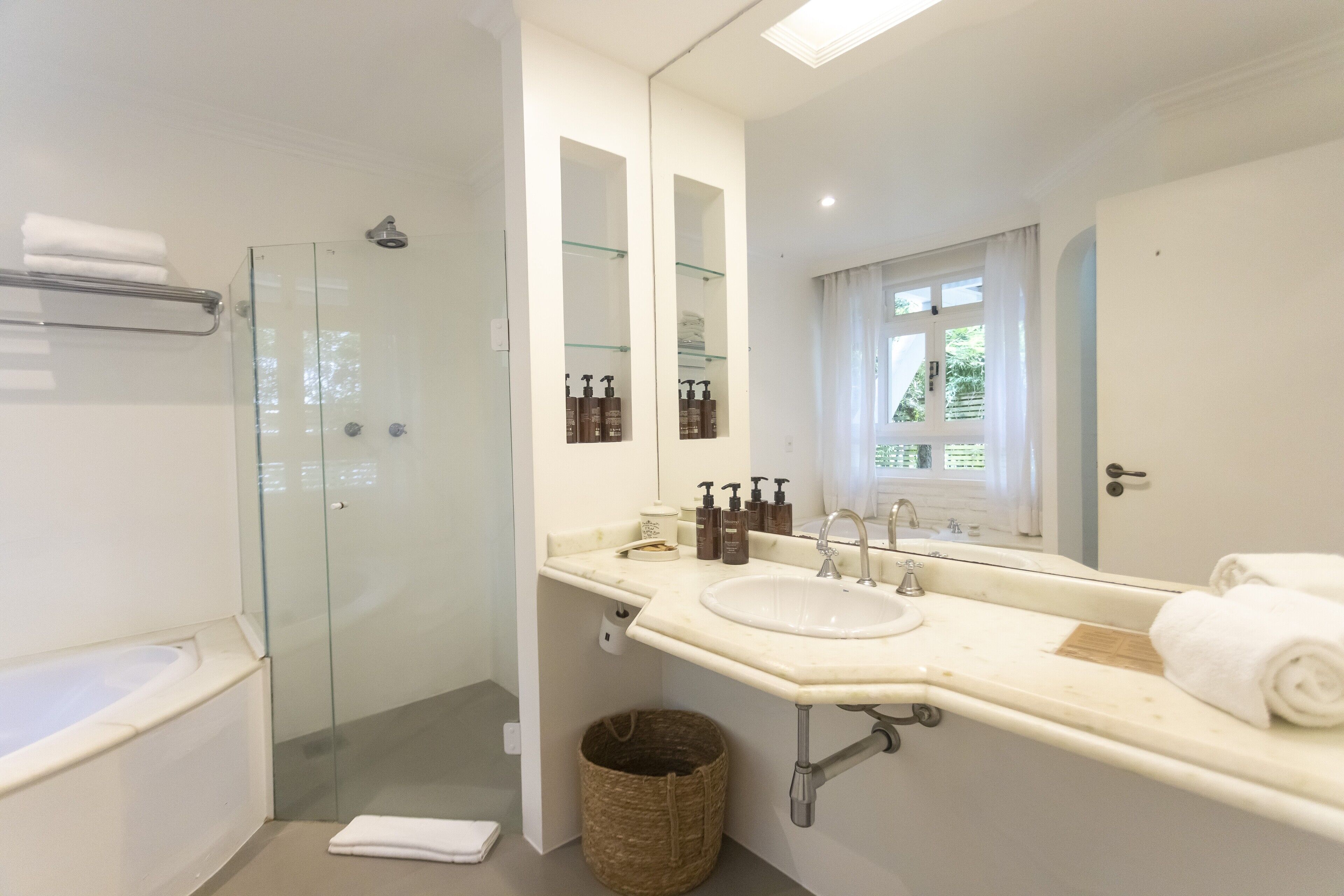 Un baño moderno con ducha de vidrio, un espejo grande y tocador con lavamanos y artículos de aseo.