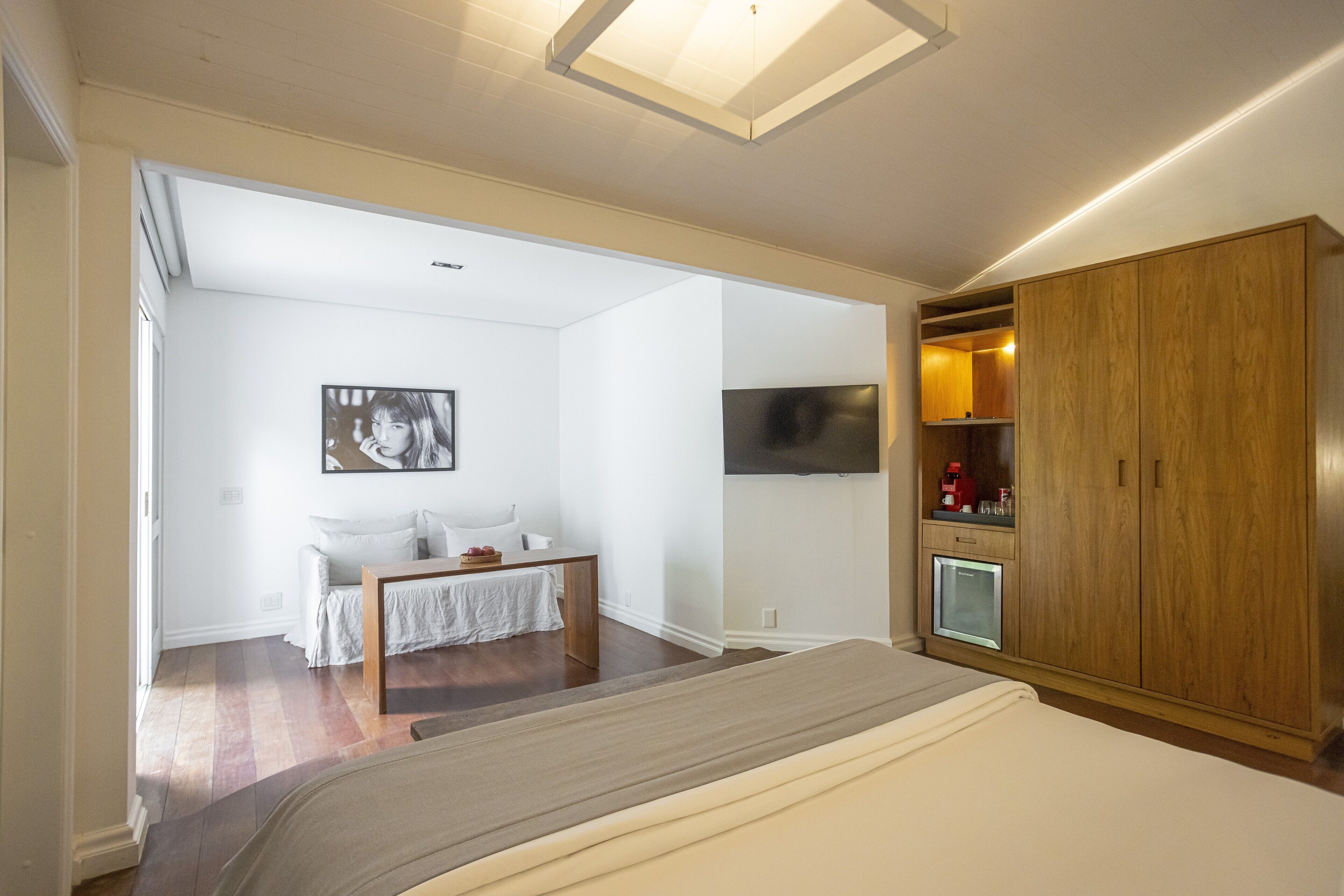 A bedroom with a bed, a wooden wardrobe, a small TV, and a desk with a chair.