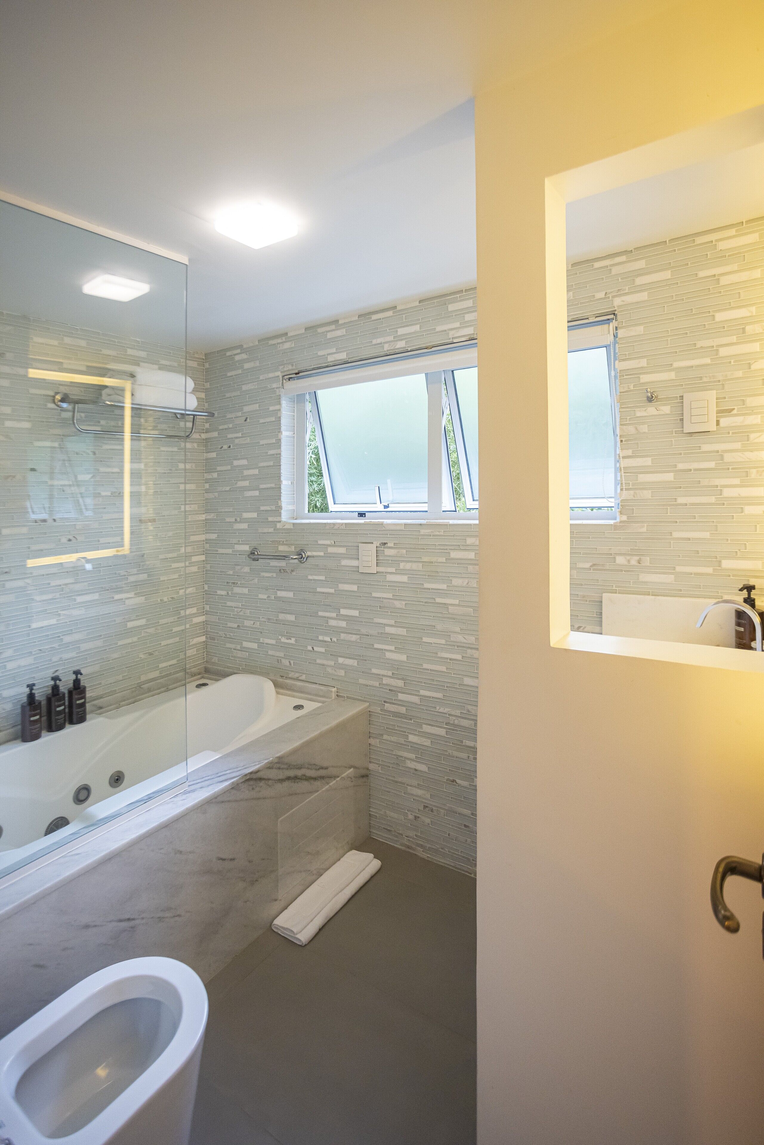 A modern bathroom with a glass-enclosed shower, a large bathtub, and a window providing natural light.