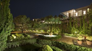 Un jardin bien éclairé, agrémenté d’une fontaine, de haies soigneusement taillées et d’un bâtiment moderne doté de grandes fenêtres.