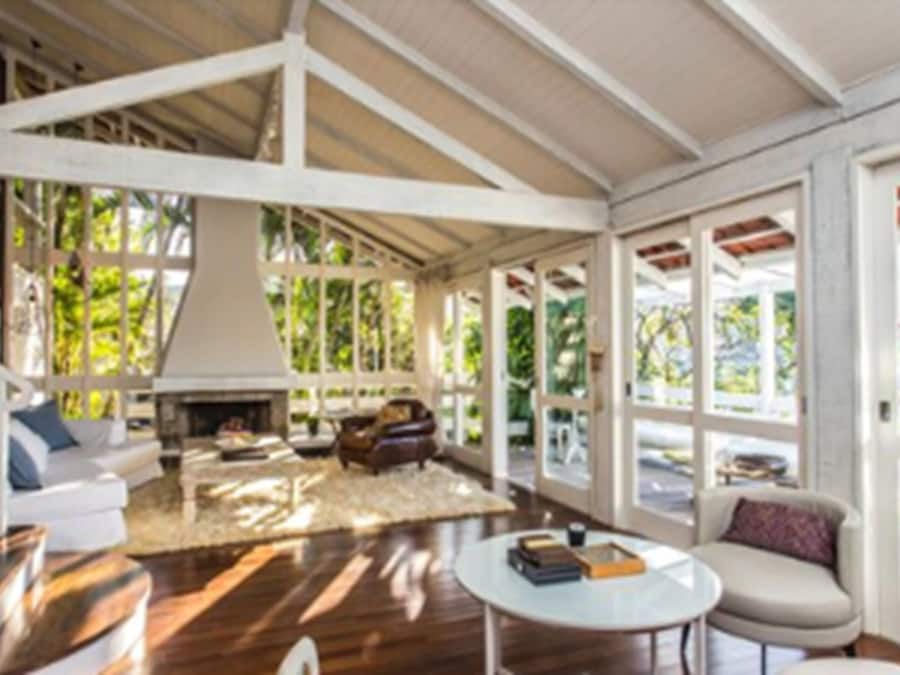 A spacious living area with a fireplace, comfortable seating, and large windows offering a view of greenery.