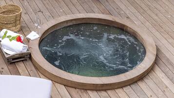 A wooden deck with a circular hot tub, a wicker basket, and a white towel with a red flower.