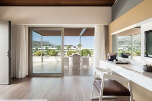 Una habitación de hotel moderna con un puerta corrediza de vidrio que da a un balcón con vistas a otros edificios de hotel y palmeras.