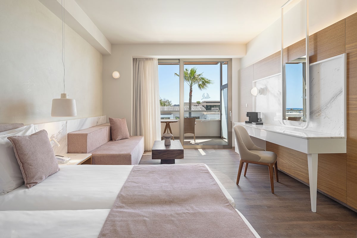 Ein modernes Hotelzimmer mit Bett, einer Couch, einem Schreibtisch und einem Balkon mit Blick.