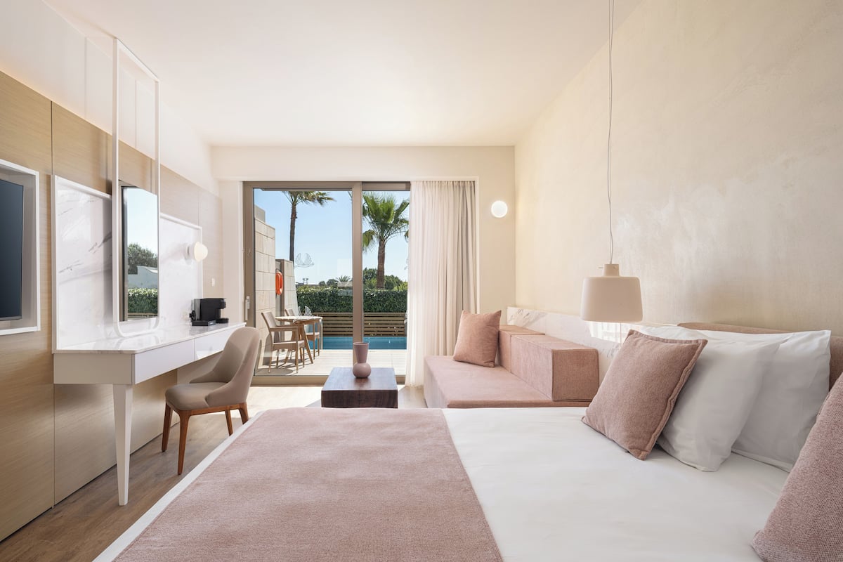 A modern hotel room with a large bed, a desk, and a view of the pool and palm trees.