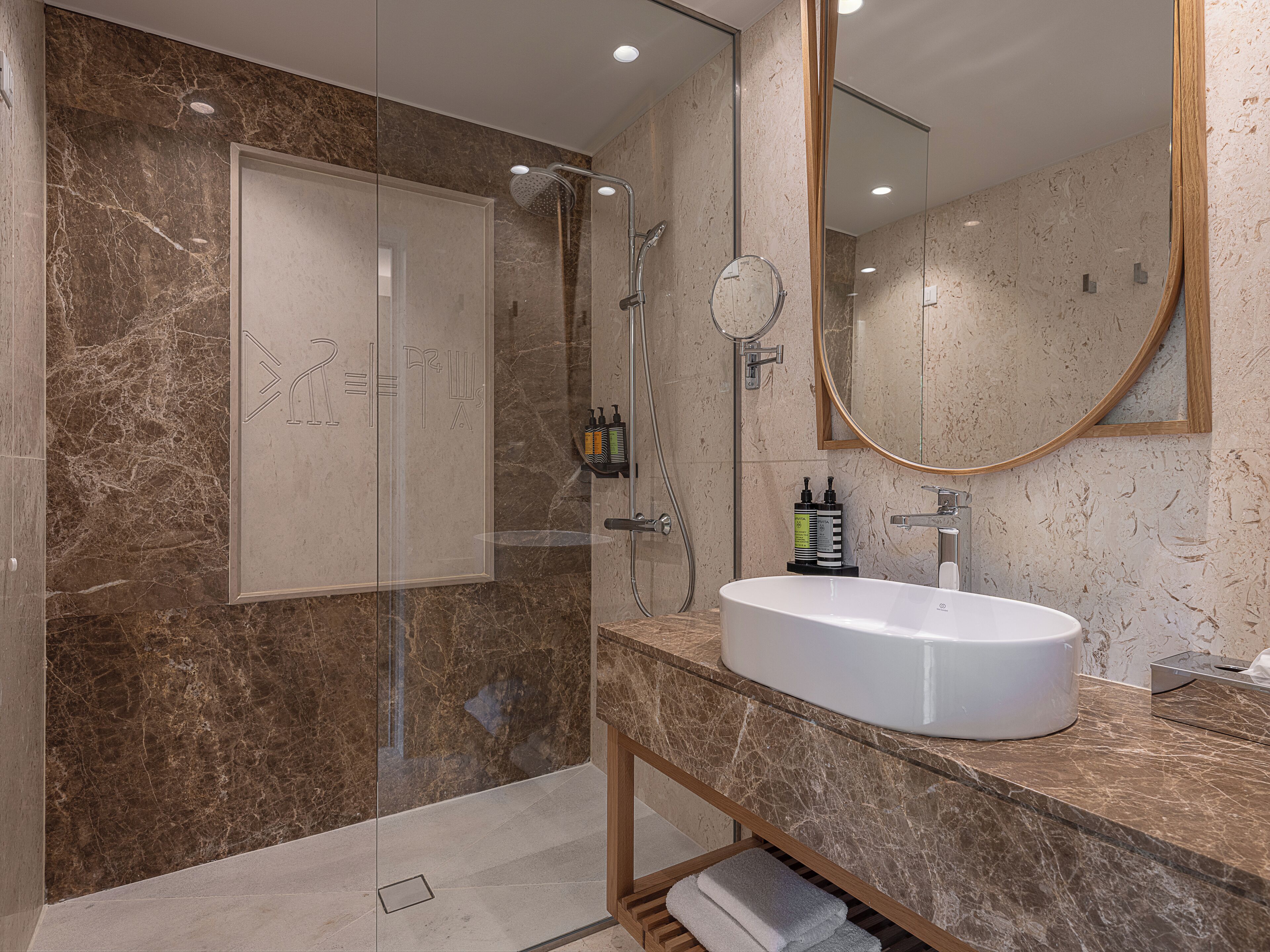 Un baño moderno con ducha envuelta en vidrio, un lavamanos blanco y pared revestida de mármol.