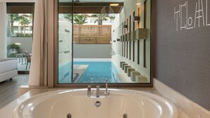 Un baño moderno con una bañera grande, zona de ducha con mampara de vidrio y vistas a una piscina y zona de estar exterior.