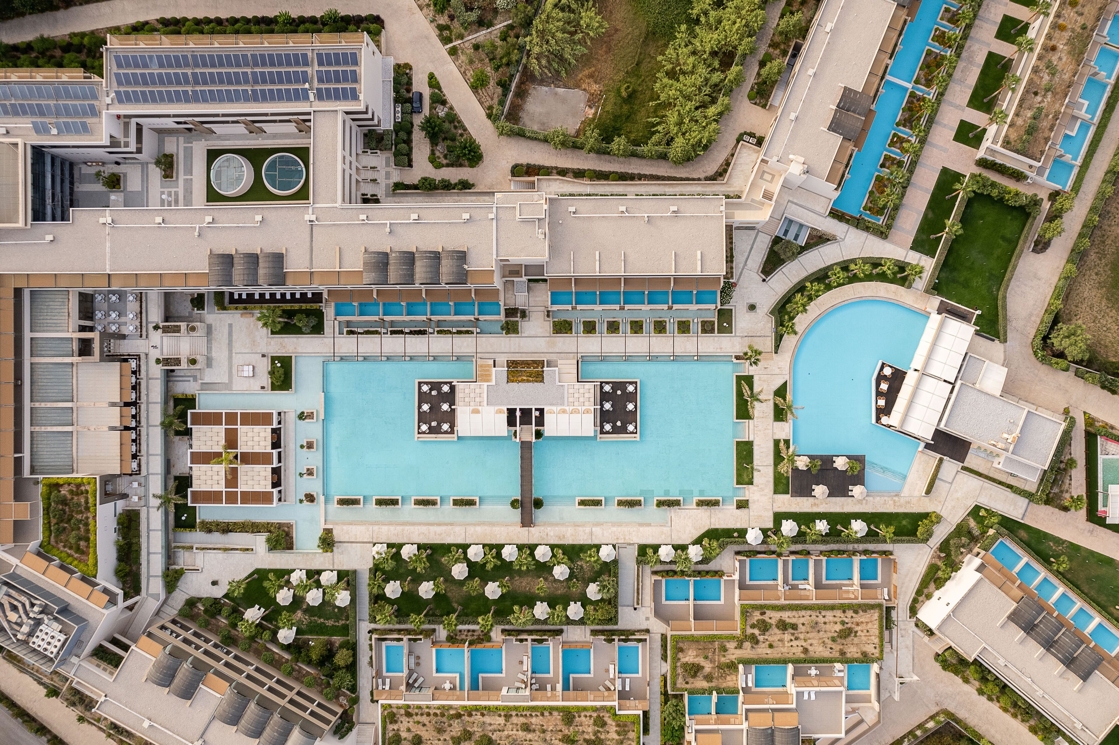 Vista aérea de un hotel con varias piscinas, un patio central y abundante vegetación.