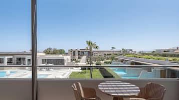 A balcony with wicker chairs and a table, overlooking a swimming pool and modern buildings.