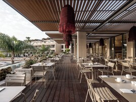 Un área de comedor al aire libre con mesas y sillas, una terraza de madera y un adorno colgante.