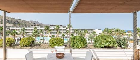 Un área de estar al aire libre cubierta con vistas a un resort, que incluye una piscina y palmeras.