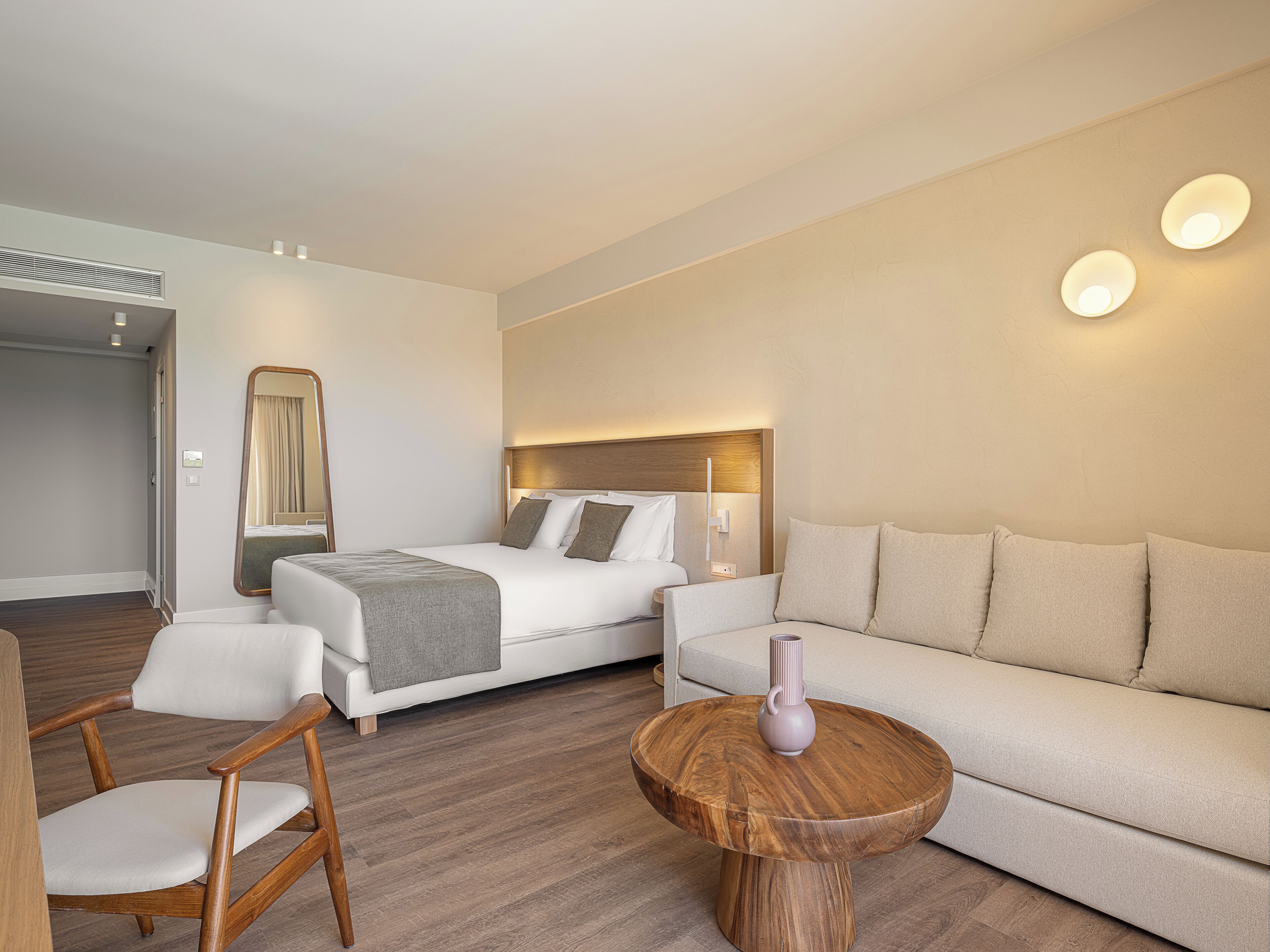 A modern hotel room with a bed, a sofa, a wooden coffee table, and a chair.