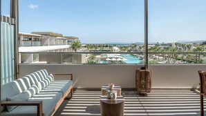 Un balcón con sofá, una mesa con taza y vistas a una piscina y edificios del resort.