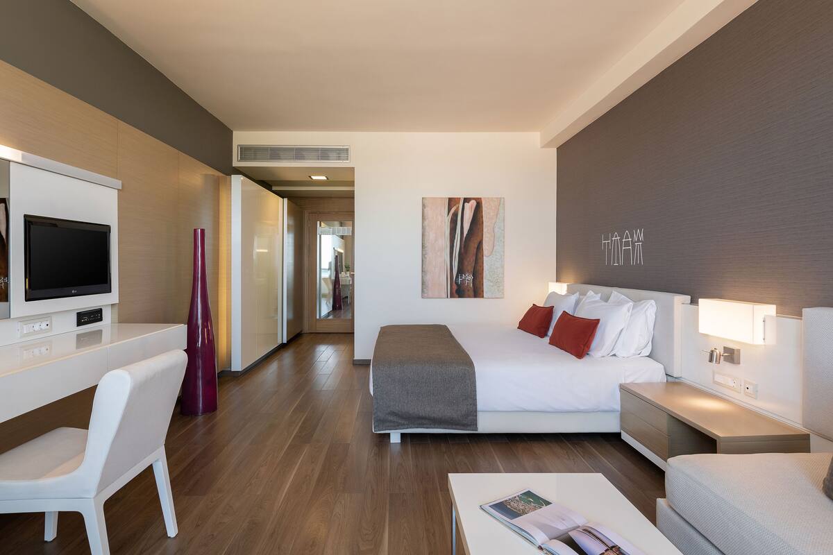 Una habitación de hotel moderna con cama, mesita de noche, televisión y un escritorio con silla.