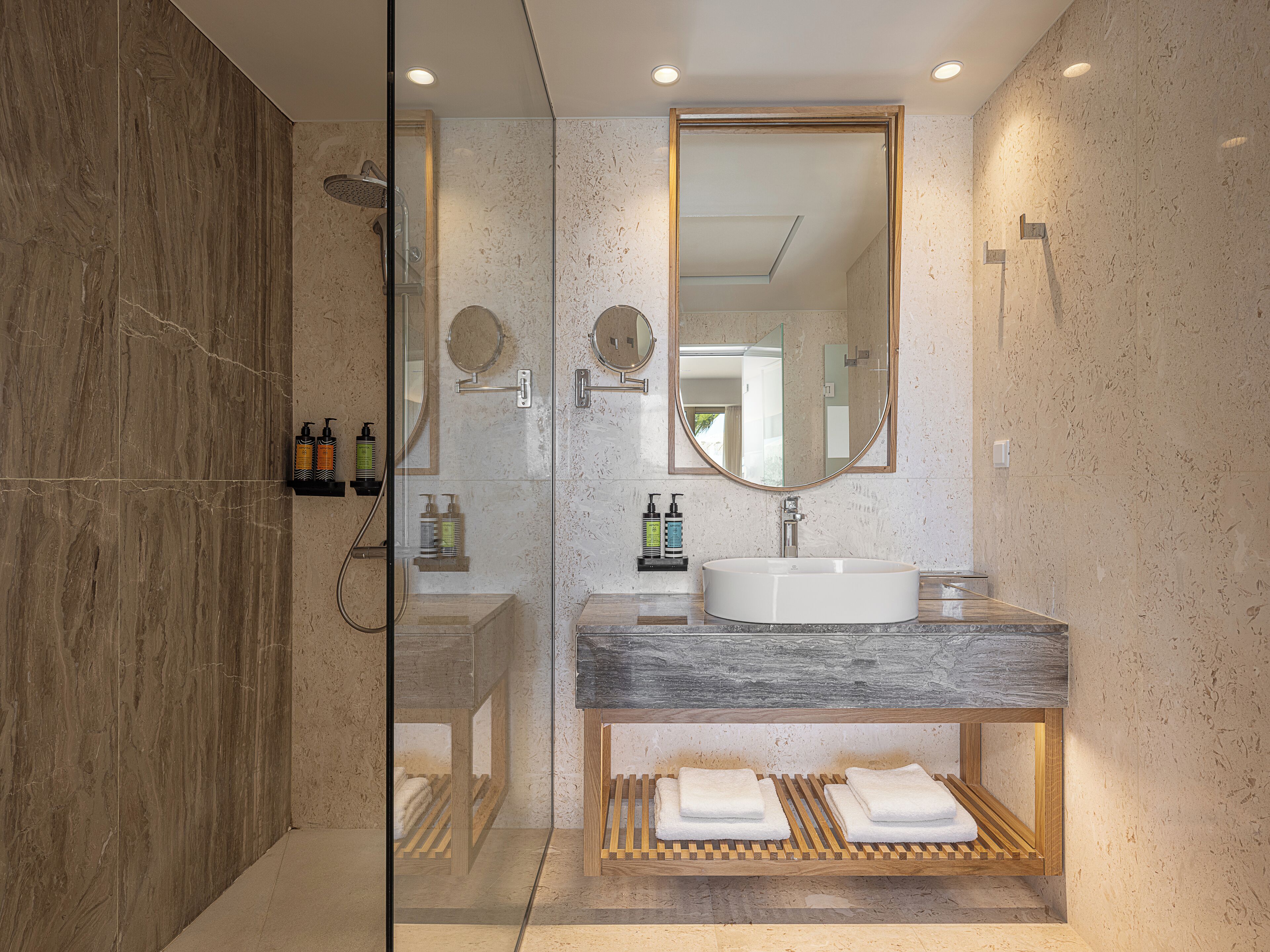 A modern bathroom with a glass-enclosed shower, a large mirror, and a marble countertop.