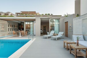 Un área de piscina moderna al aire libre con sillones de descanso, una mesa y un sofá.