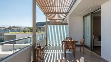 Un balcón con una pérgola de madera, barandilla de vidrio y zona de estar con mesa y sillas.
