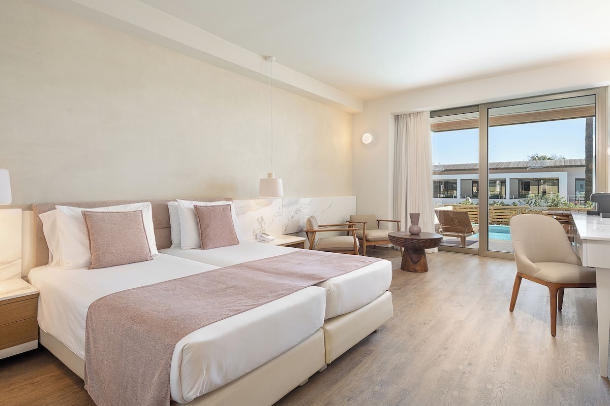 A modern hotel room with a large bed, a desk, and a view of the pool area.