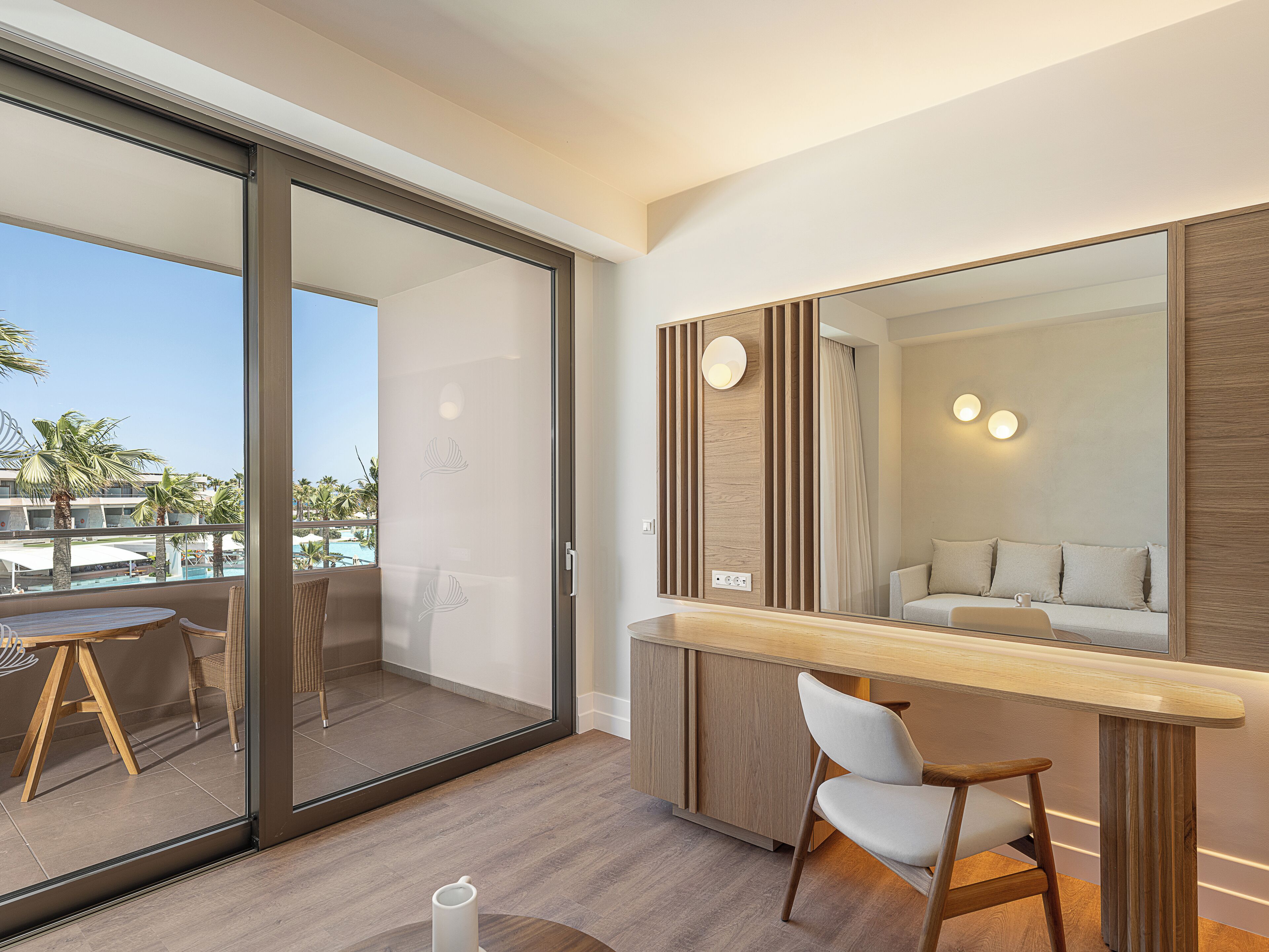 A modern bathroom with a large mirror, wooden paneling, and a view of a pool and palm trees through a sliding glass door.
