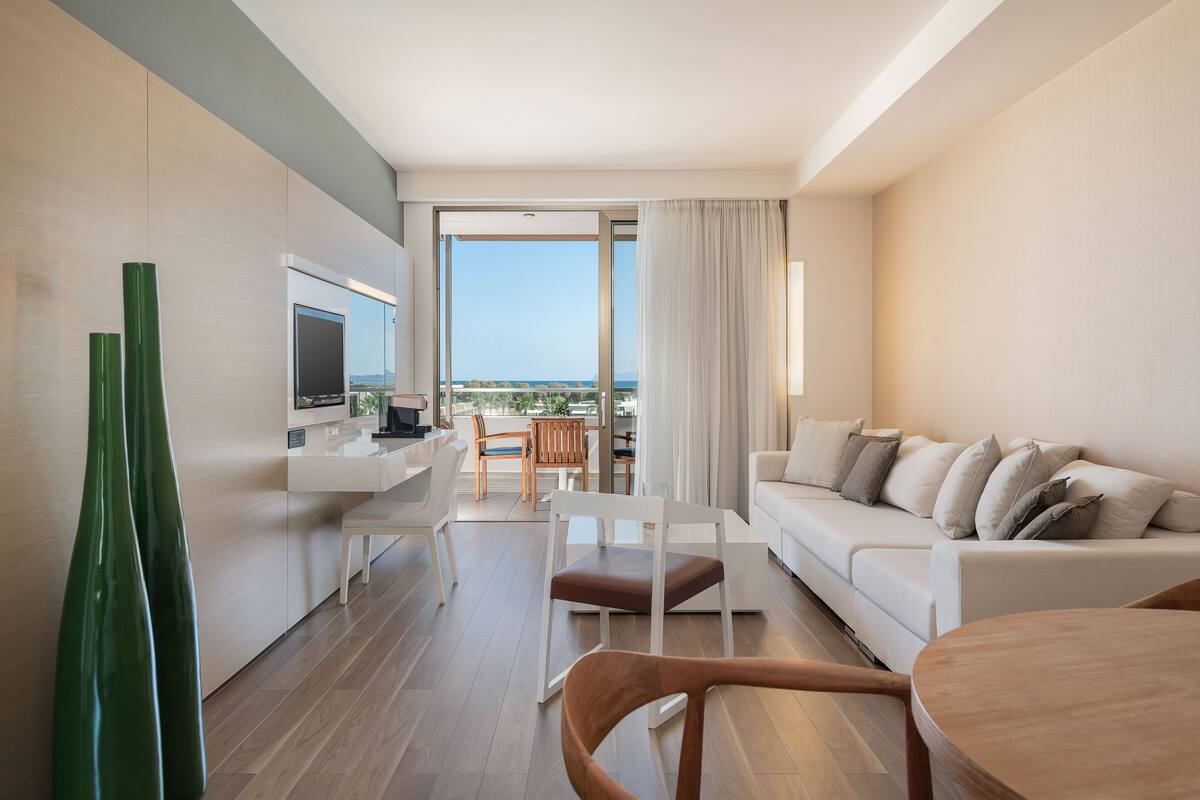 Una habitación de hotel moderna con balcón, sofá, mesa de comedor y televisor.