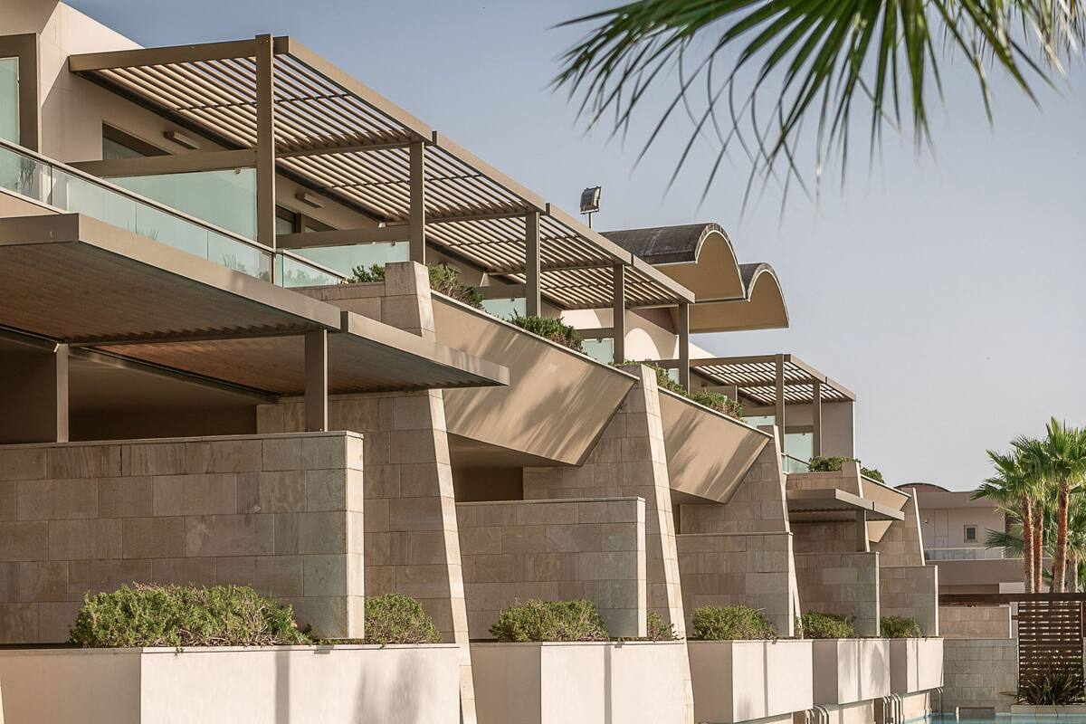 Un hotel moderno con piscina, varios balcones y cielo despejado.
