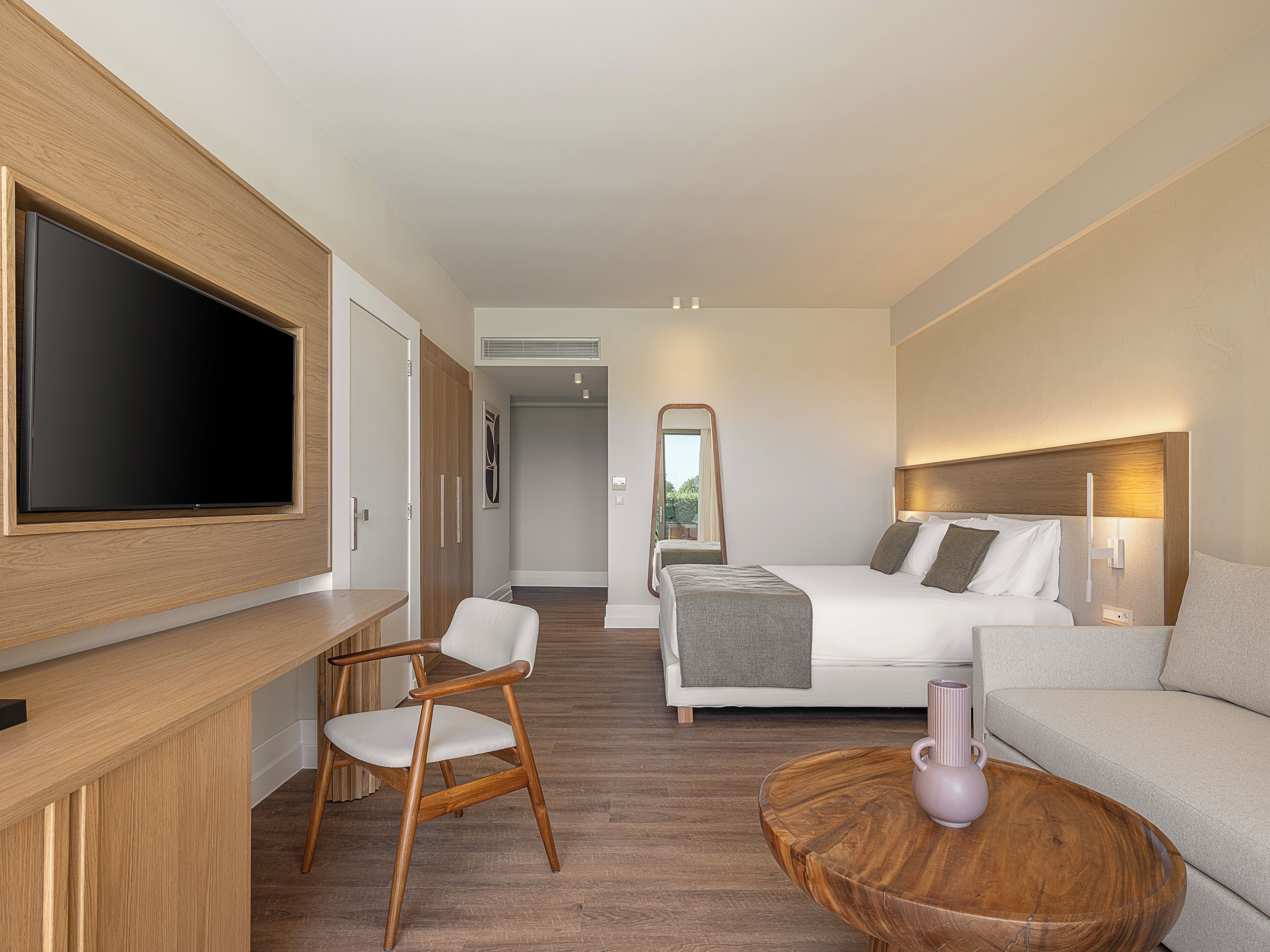 A hotel room with a TV, a bed, a sofa, a chair, and a wooden coffee table.