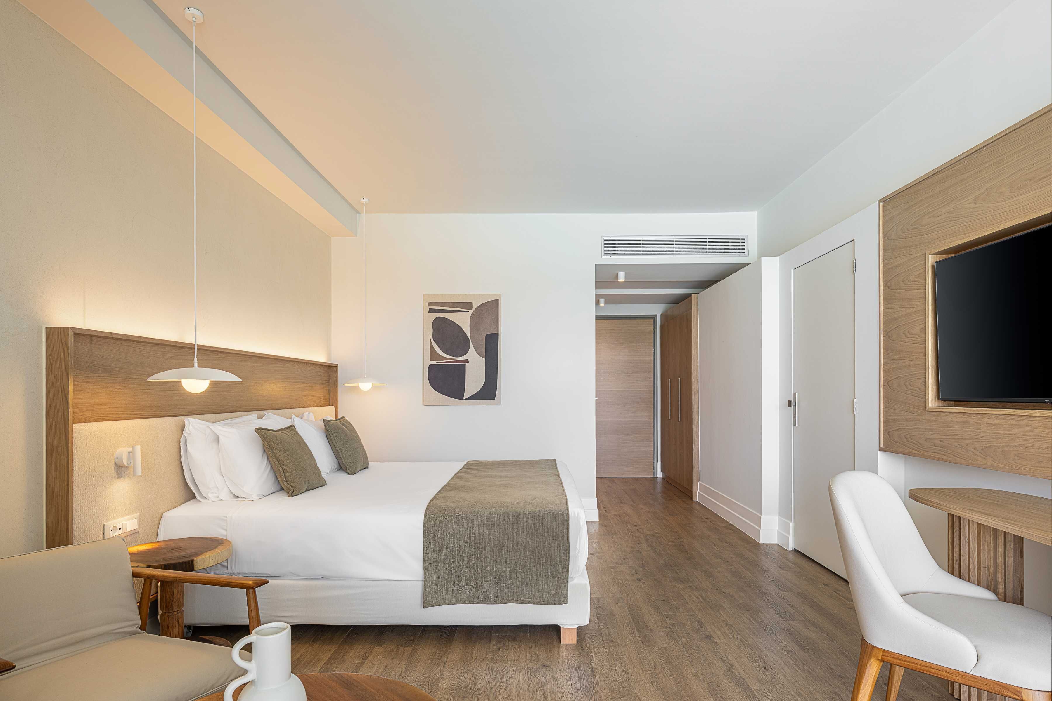Una habitación de hotel moderna con cama, mesita de noche, silla y televisor fijado a la pared.